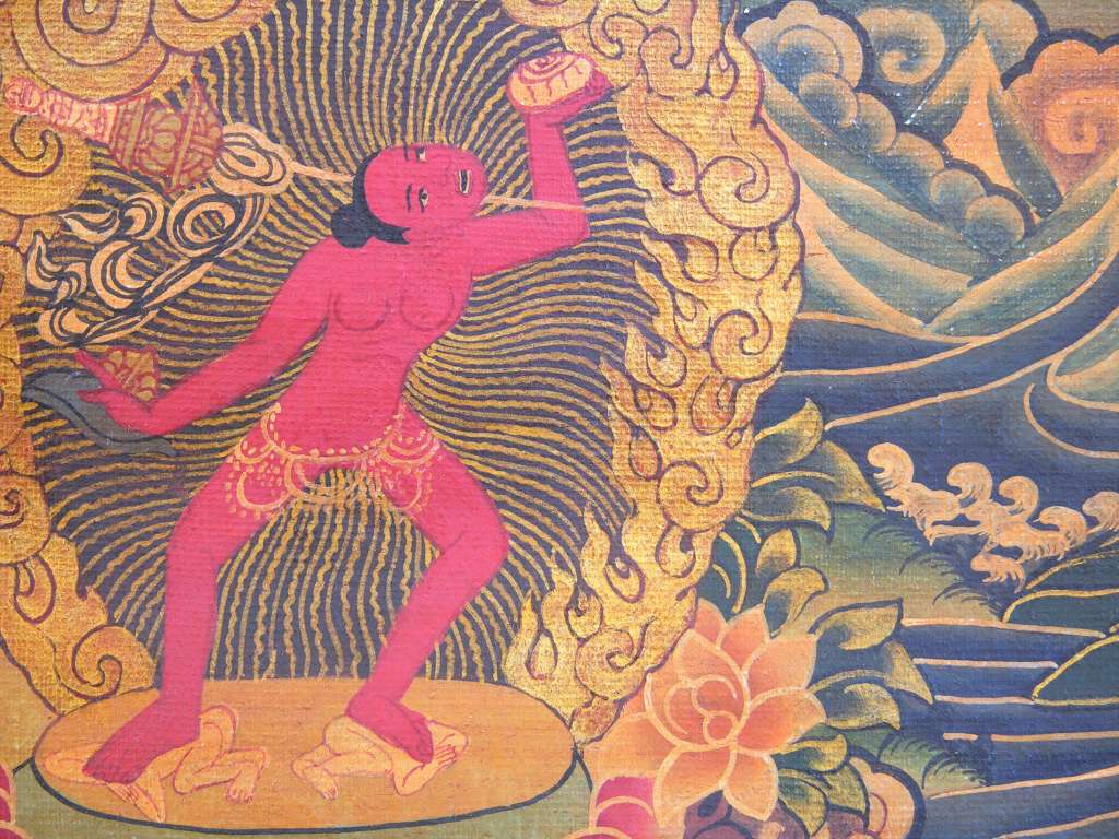 Chakrasamvara Mandala 05-1 Bottom Left - Vajrayogini Below the mandala on the left is Vajrayogini (Tib. Naro Khachoma), the dakini of wisdom. Vajrayogini is visualized as a red-coloured 16-year old girl, in the full bloom of her youth, radiantly beautiful, full of freshness and vitality. Her intense expression reflects her passionate nature. She carries a knife in her right hand and a skull cup in her left hand and a bone khatvanga on her shoulder. She symbolizes the female tantric aspect of the Buddha embodying the union of bliss and emptiness. Her naked red body represents the transformation of passion and sexual energy into compassion.